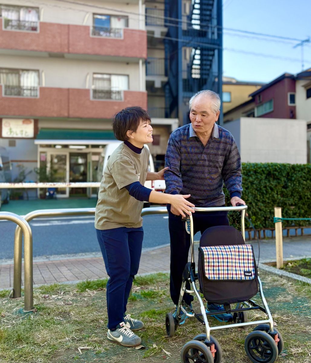 歩行器を押して街を歩く男性と、隣で見守るスタッフ